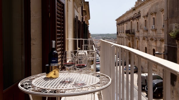 A balcony with a round table, two wine glasses, and a bottle of wine. - Elegant apartment, in the heart of the historic center of Noto, for 2 to 6 guests (Noto)