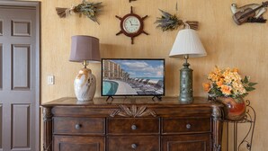 Un comò in legno con una televisione che mostra una spiaggia, una sveglia e oggetti decorativi al muro.
