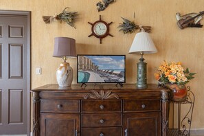 A wooden dresser with a television displaying a beach scene, a clock, and decorative items on the wall.