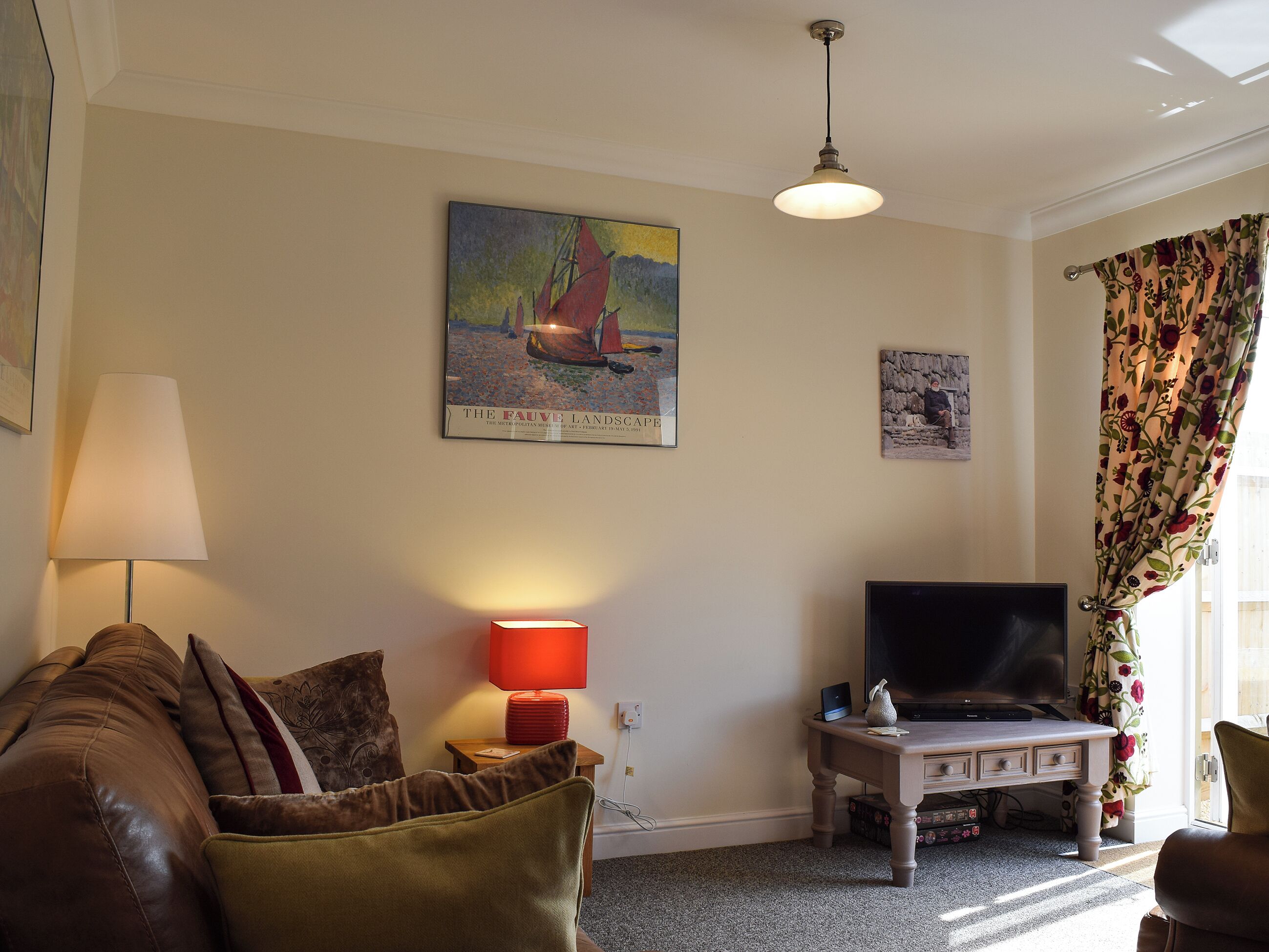 A living room with a sofa, a table with a lamp, a television, and artwork on the wall.