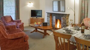 A living room with a fireplace, a television, and a dining area set for a meal. - 2 bedroom accommodation in Lostwithiel (Lostwithiel)