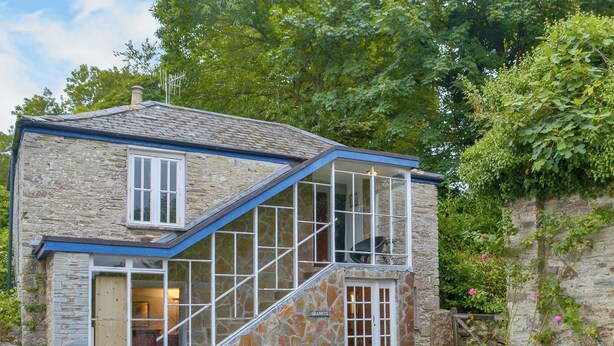 A stone house with a sloped roof, a large bay window, and a staircase leading to the upper floor. - 2 bedroom accommodation in Lostwithiel (Lostwithiel)