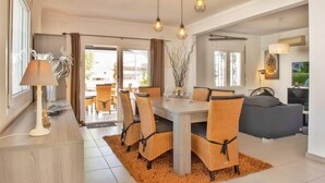 Un coin repas avec des chaises en osier, une table et une lampe. Le salon comprend un canapé et un téléviseur.