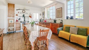Een ruime keuken met houten kastjes, een eettafel en een gele bank.