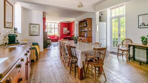 Een ruime keuken met houten kastjes, een eettafel voor vier personen, en een rode woonkamer op de achtergrond.