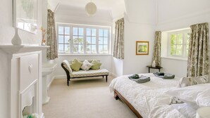 Een slaapkamer met een groot raam, een bed, een bankje en een dressoir.