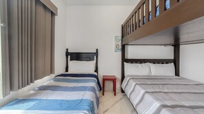 Een kamer met twee bedden, waarvan één met een gestreept dekbed en de andere met een effen. Er staat een klein rode tafel tussen de bedden.