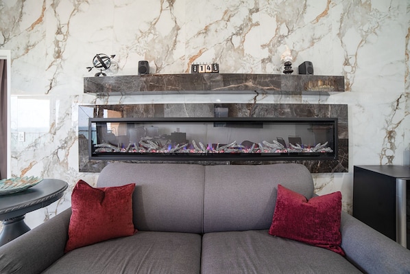 Ein Wohnzimmer mit einer Couch, zwei roten Kissen, einem Kamin mit Glaseinsatz und einer Marmorwand.