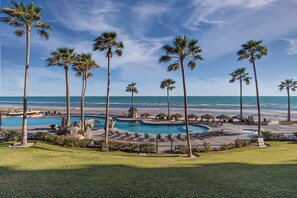 Een resort met meerdere zwembaden, palmbomen en uitzicht op het strand.