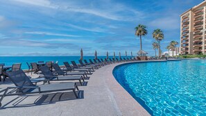A resort pool with lounge chairs and palm trees, overlooking the ocean.
