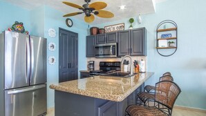 A kitchen with dark cabinets, a stainless steel refrigerator, a microwave, and a granite countertop. - Sonoran Sea East 711 Beautiful Spacious Ocean View Condo (Puerto Peñasco)