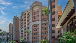 A multi-story hotel with balconies, a central courtyard, and palm trees.
