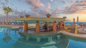 A poolside area with lounge chairs, a covered seating area, and a view of the sea at sunset.
