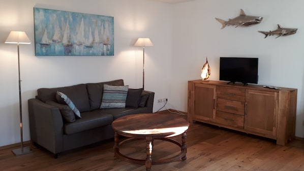 A living room with a sofa, a coffee table, a TV on a wooden cabinet, and a painting of sailboats on the wall.