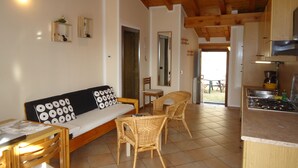 Une pièce chaleureuse avec un canapé, des fauteuils en osier, une table à manger et un coin cuisine.