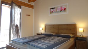 Une chambre à coucher avec une tête de lit en bois, deux tables de chevet avec des lampes, un lit avec une literie à rayures, une fenêtre avec des rideaux et un tableau floral accroché au mur.