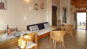 Une pièce chaleureuse avec une table en bois, des chaises, un canapé agrémenté de coussins à motifs et une porte donnant sur un espace extérieur.