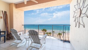 Un balcón con dos sillas Adirondack, una mesita y vistas a la playa y al océano.