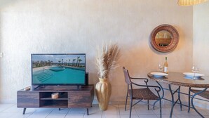 Habitación con televisión mostrando vista a la piscina, mesa de comedor con sillas, jarro con plumas de pampa y espejo en la pared.