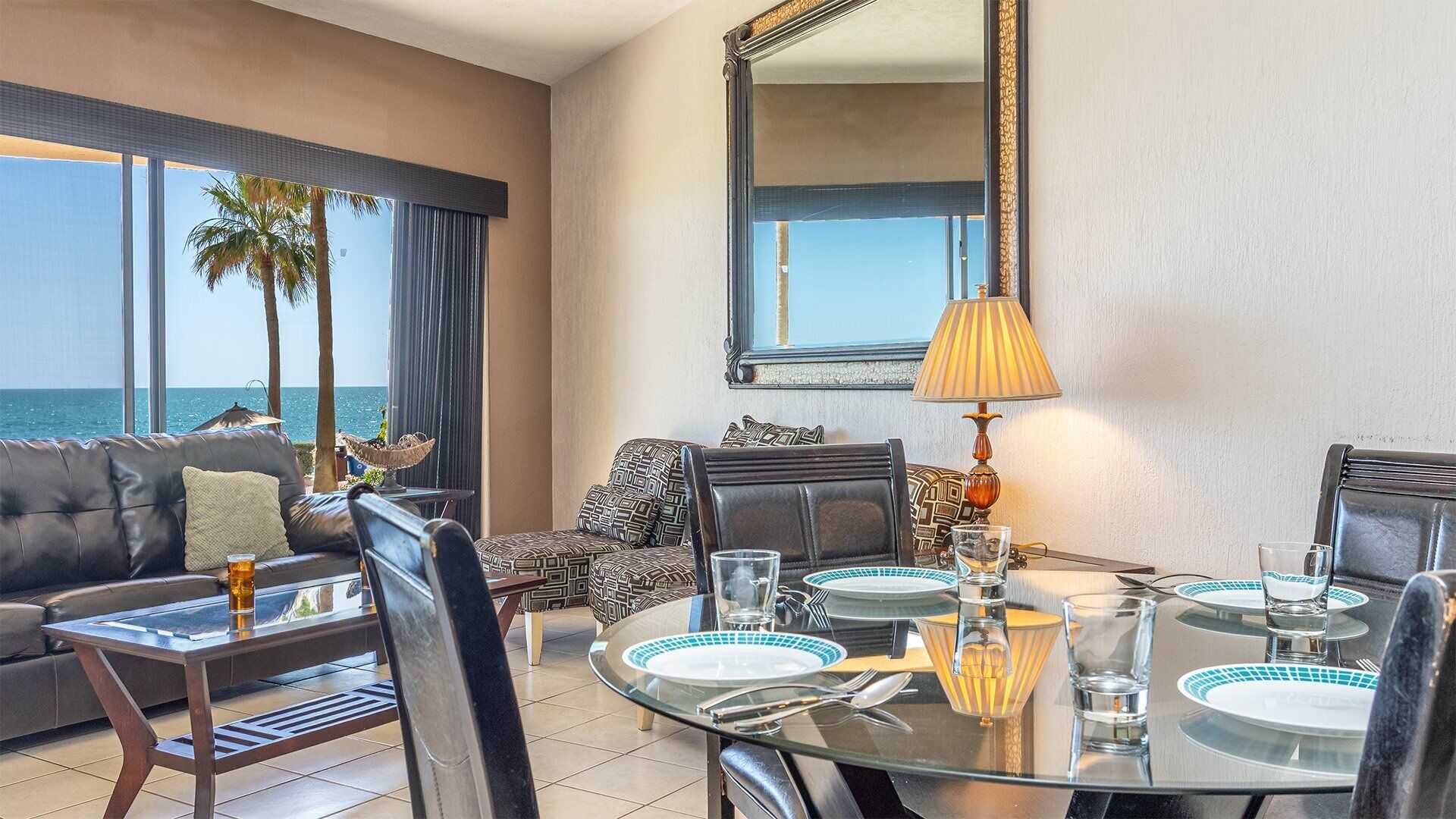 Une chambre d’hôtel avec une table à manger dressée pour quatre personnes, un canapé, un fauteuil et une grande fenêtre donnant sur l’océan.