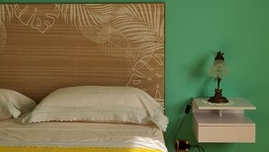 A bed with a yellow bedspread, white pillows, and a white blanket. There is a bedside table with a lamp and a power outlet. The wall is green, and there is a decorative branch on the wall. - Renovated and equipped apartment in Cervia-Milano Marittima (Cervia)