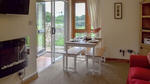 Zona pranzo con tavolo apparecchiato per due, televisione a parete e vista all'esterno tramite una porta in vetro.