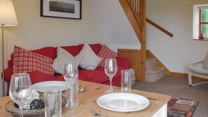 Un'area pranzo con un tavolo in legno apparecchiato per due, un divano rosso con cuscini decorati, un quadro appeso alla parete e una scala con ringhiere in legno.