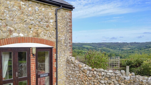 Un edificio in pietra con un ingresso in mattoni, una targa che recita “THE SMITHY” e vista su dolci colline sullo sfondo.