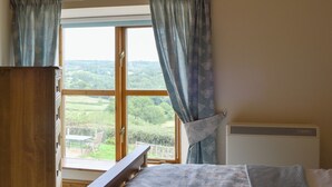 Una camera da letto con un letto di legno, una finestra con tende e vista sul verde circostante.