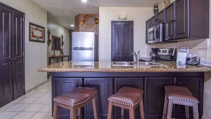 A kitchen with dark cabinets, a stainless steel refrigerator, a sink, and three stools.