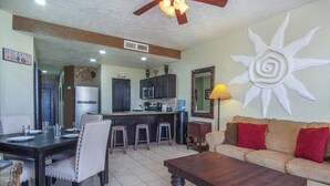 A living room with a sofa, coffee table, and dining area with chairs and a kitchen in the background.
