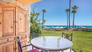 A patio with a table and chairs, a wooden cabinet, and a view of the beach with palm trees and umbrellas.