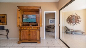 A living room with a wooden entertainment center, a television displaying a beach scene, a sofa, and a decorative sun wall. - Sonoran Sea E-805 Barefoot @ Sea Retreat Stunning Oceanfront Condo (Puerto Peñasco)