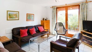Un salón con sofá, sillón, una mesa de centro de cristal y televisor sobre un mueble de madera.