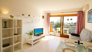 Una sala moderna con televisor, comedor y balcón con mobiliario exterior.
