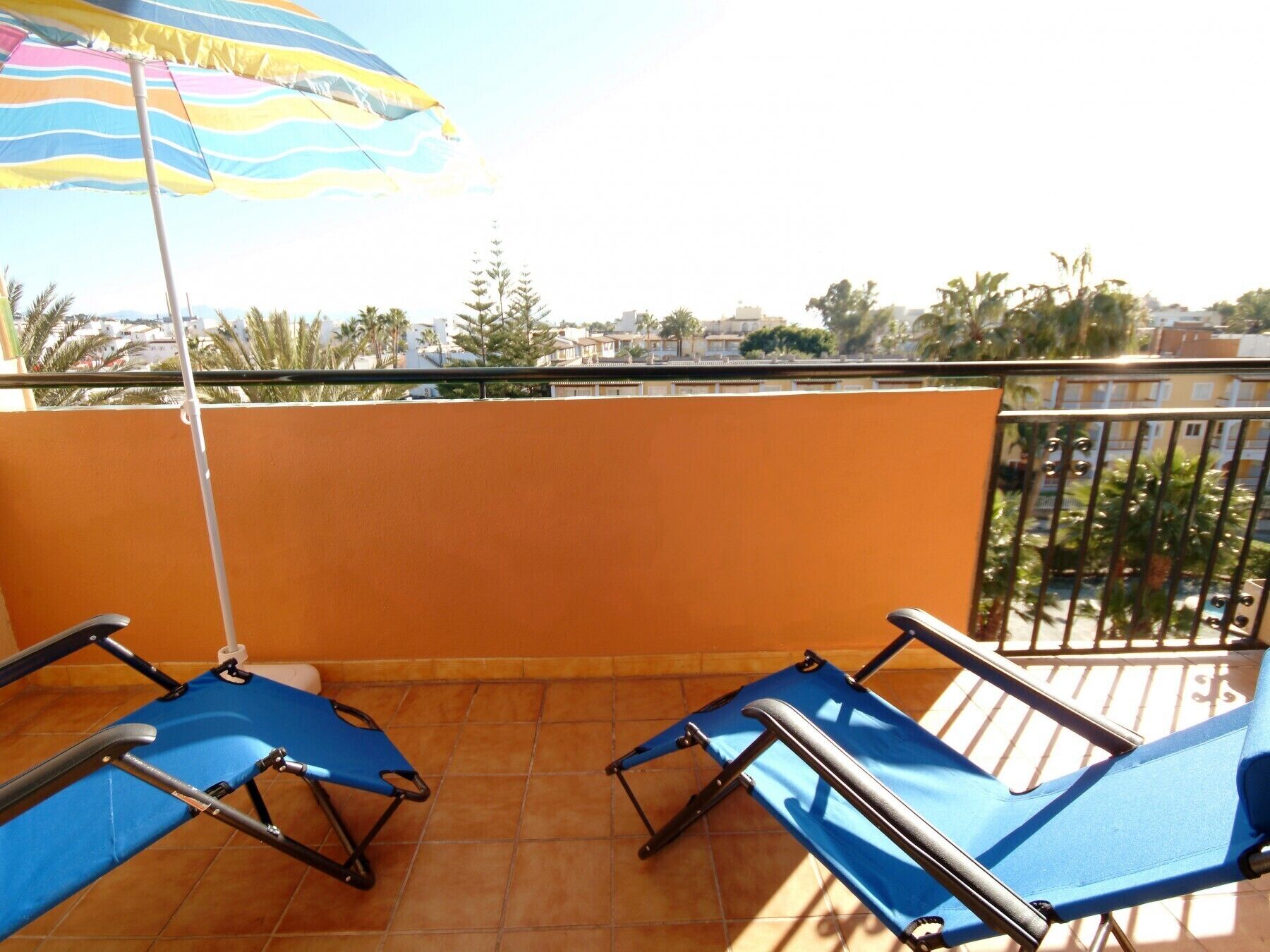 A balcony with two blue lounge chairs and a striped umbrella.