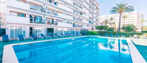 A hotel with a swimming pool, multiple balconies, and palm trees.