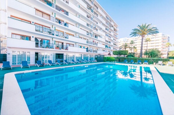 A hotel with a swimming pool, multiple balconies, and palm trees.
