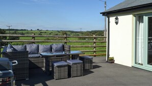 Un espace extérieur aménagé avec des meubles en osier, un barbecue et une vue sur la campagne.