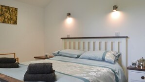 Un lit bien fait, avec une tête de lit, deux tables de chevet avec des lampes, un petit tableau accroché au mur et un banc en bois.