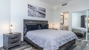 A bedroom with a bed, bedside tables, a nightstand, a mirror, and a bathroom visible through an open door.