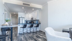 A modern kitchen with white cabinets, a stainless steel refrigerator, and a bar area with black chairs.