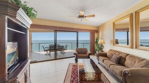 A living room with a balcony overlooking the sea, furnished with a sofa, armchair, and dining table.