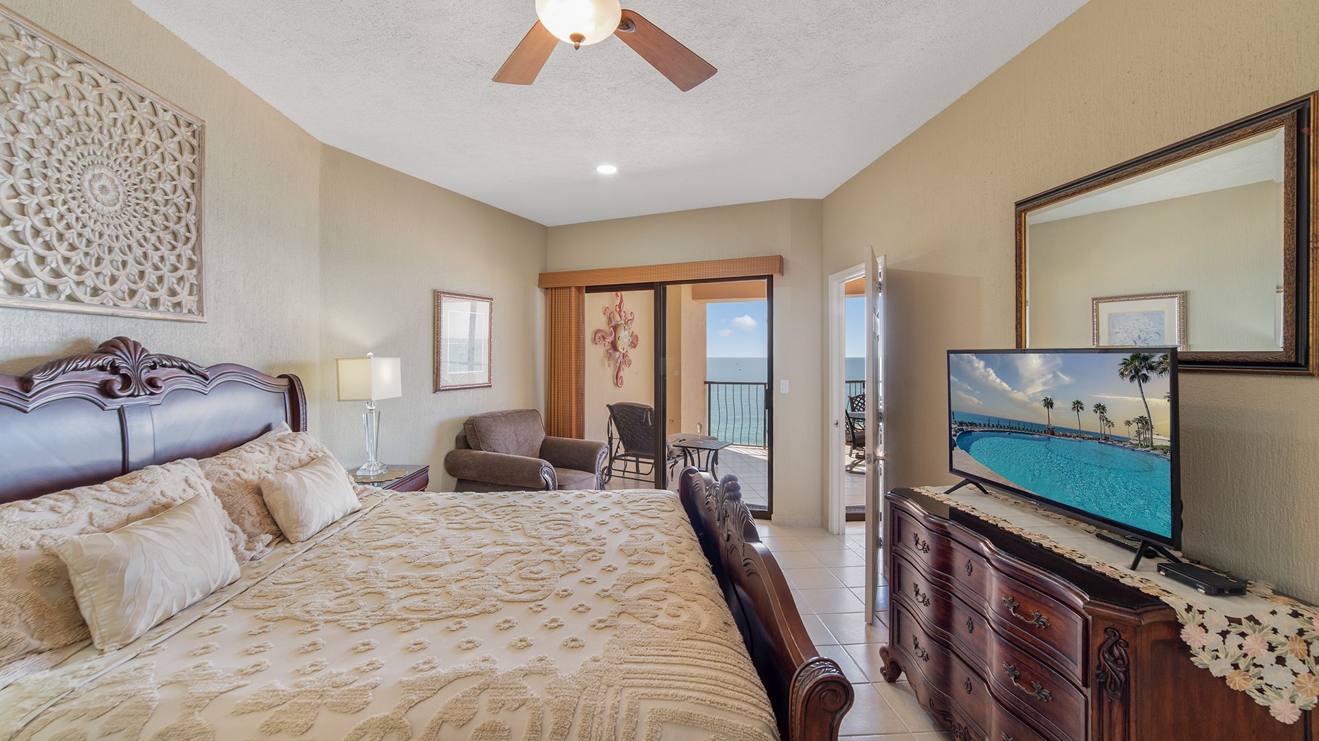 A hotel room with a large bed, a television, a dresser, and a balcony with a view of the ocean.