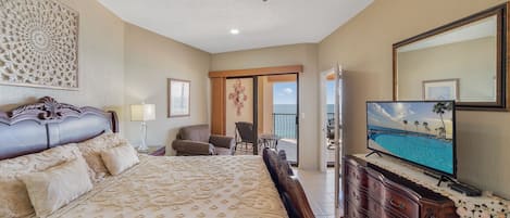 A hotel room with a large bed, a television, a dresser, and a balcony with a view of the ocean.