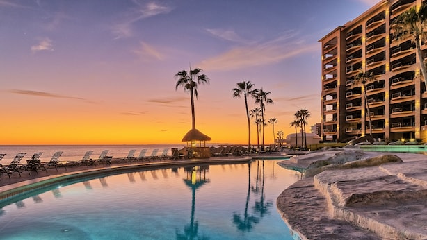 A resort pool with lounge chairs and palm trees, a building with multiple balconies, and a sunset view. - Sonoran Sea E-605 Barefoot By The Sea Wonderful Oceanfront (Puerto Peñasco)