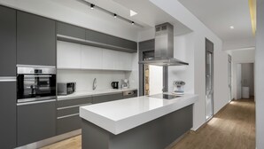 Una cocina moderna con armarios grises, una isla con encimera blanca, electrodomésticos de acero inoxidable y piso de madera.
