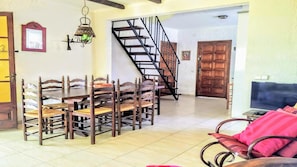 A dining area with a wooden table and chairs, a staircase, and a television in the living room.