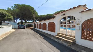 Una proprietà recintata con piscina, un'auto parcheggiata di fronte e un edificio con finestre ad arco e tetto in tegole.