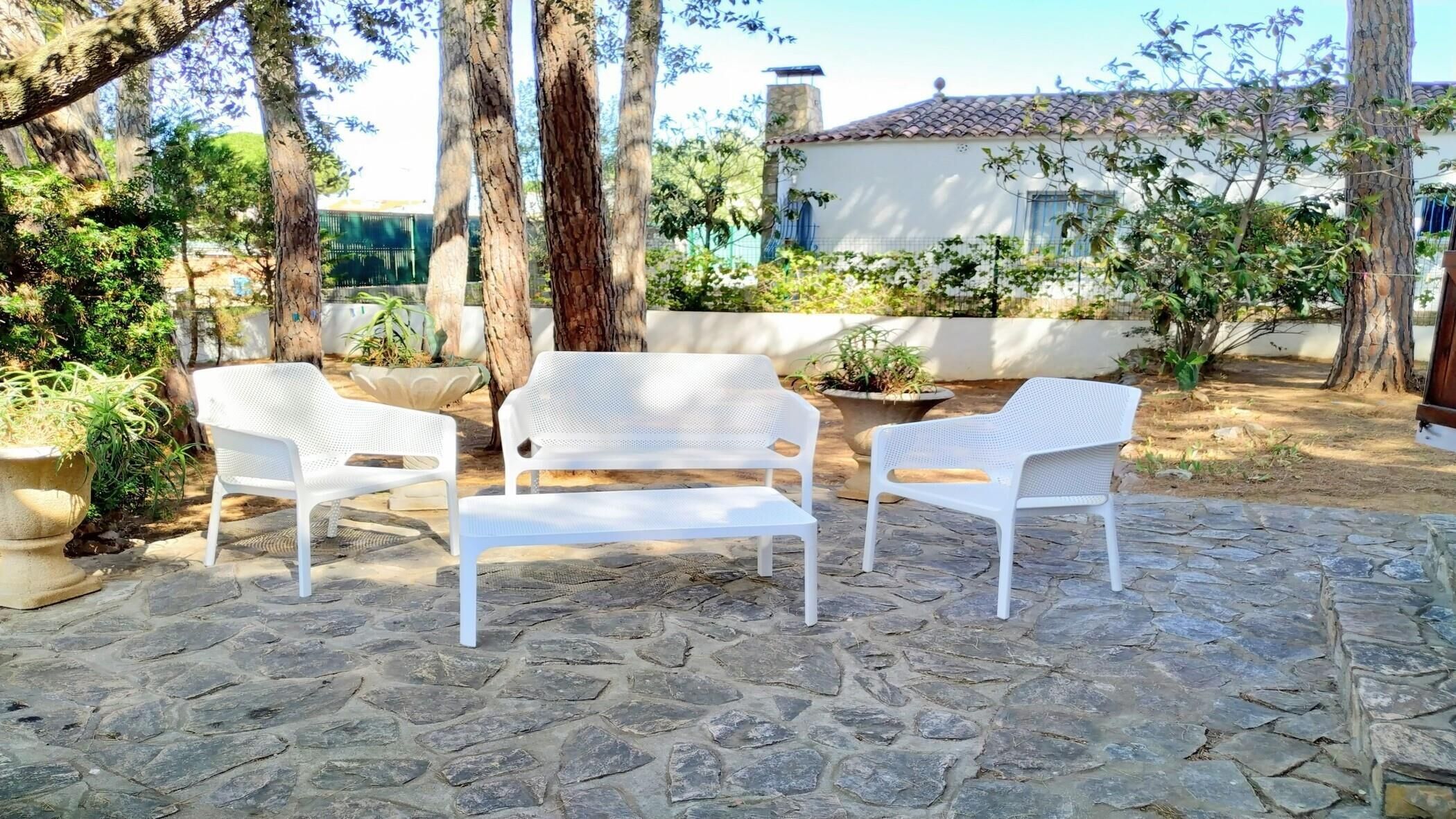 A patio with stone flooring, white plastic chairs, and potted plants.